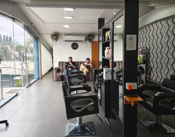 The salon's waiting area with a sofa, wall fans and the HM logo, beside the glass frontage